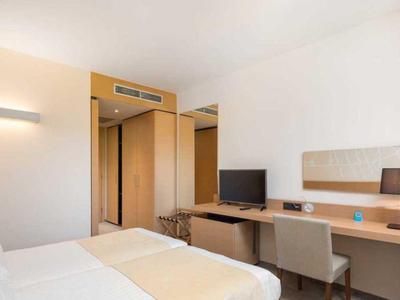 Jasny pokój hotelowy z łóżkiem, biurkiem, krzesłem, telewizorem i szafą.