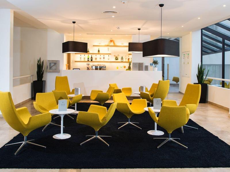 Nowoczesna strefa wypoczynkowa z żółtymi fotelami i białymi stolikami na czarnym dywanie.