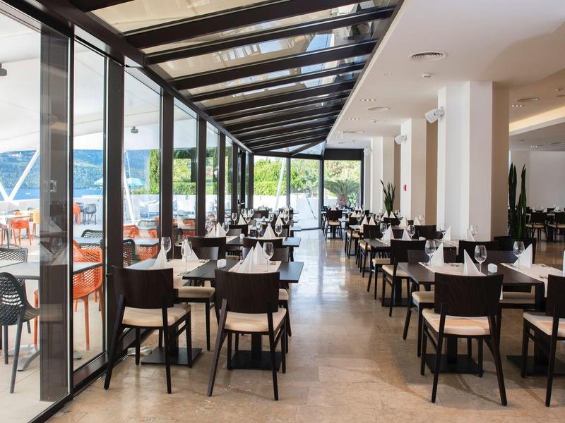 Nowoczesna jadalnia z stołami i krzesłami, przylegająca do tarasu z widokiem na zewnątrz.