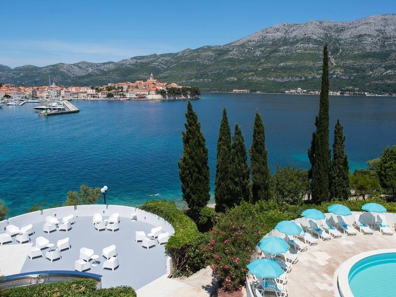 Widok na teren basenu z leżakami i morzem w tle pod czystym niebem.