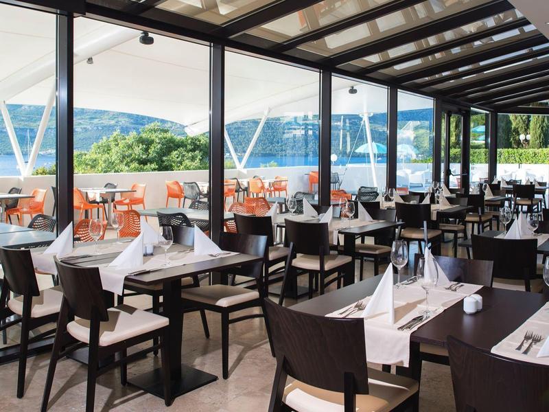 Nowoczesna restauracja z dużymi oknami i tarasem z widokiem na rzekę i zielone wzgórza.