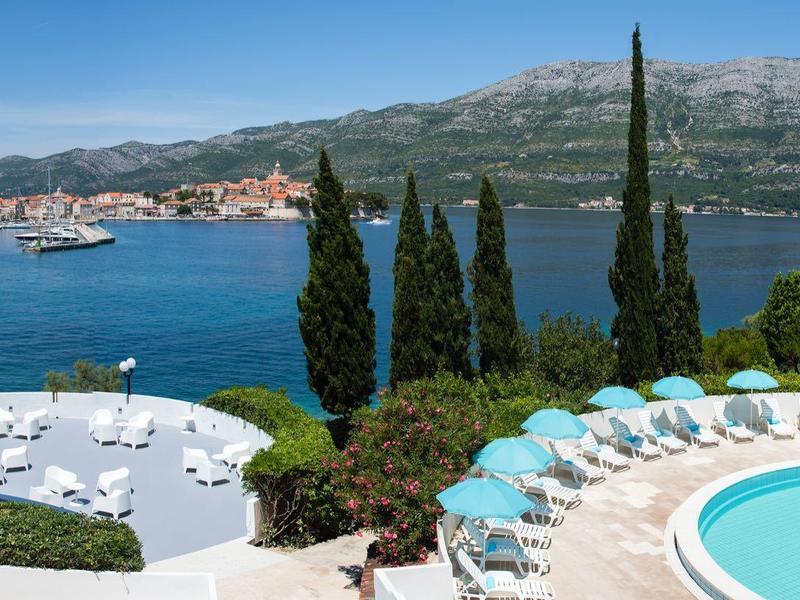 Basen z leżakami przy zatoce z górami i cyprysami