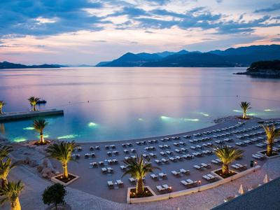 Moderne Wohnanlage mit Balkonen, umgeben von Palmen und grasbewachsenen Flächen bei Abenddämmerung.