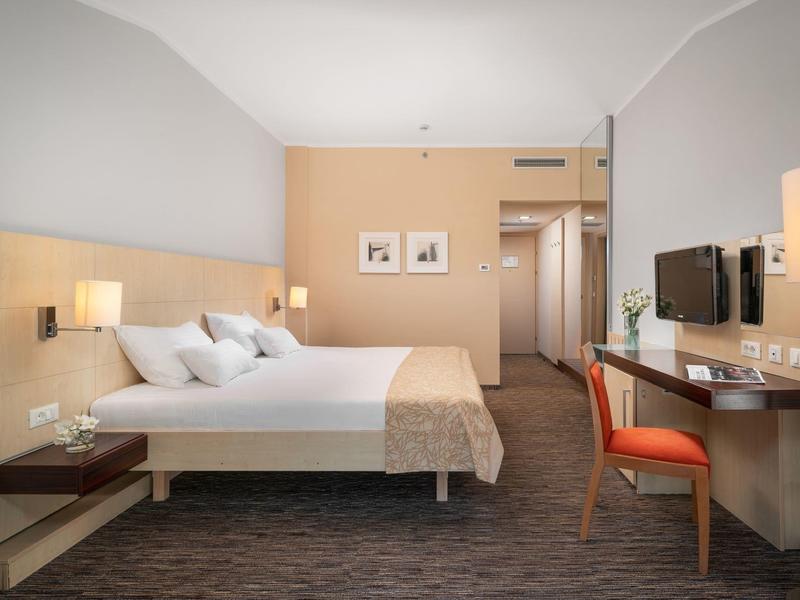 Modern hotel room with double bed, desk, chair, and neutral color scheme.