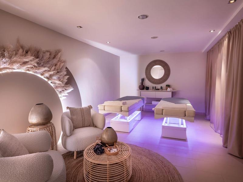 A modern, calming spa room with two loungers, soft lighting, and cozy seating areas.