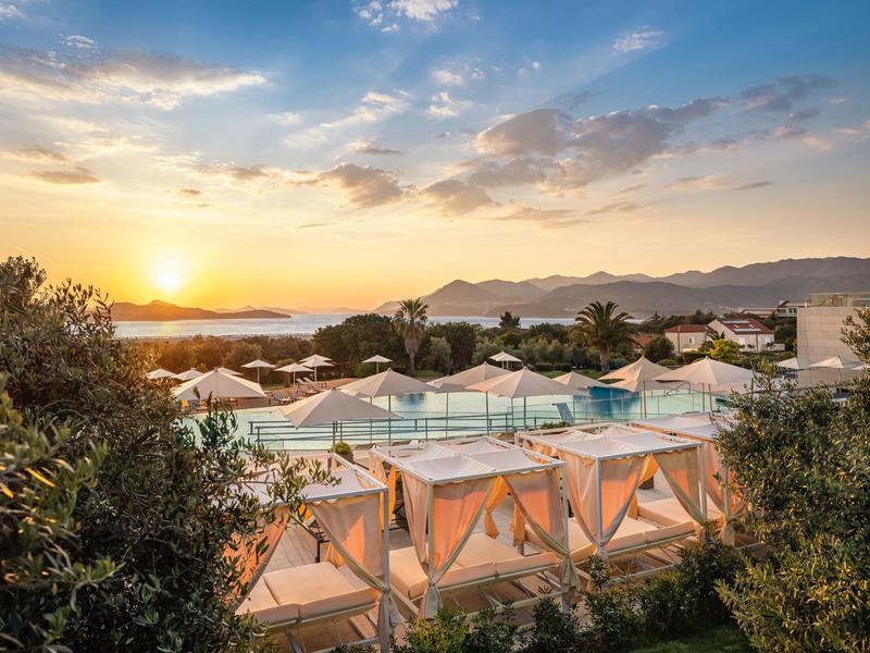 Sunset over a pool area with white loungers and palm trees at a resort.