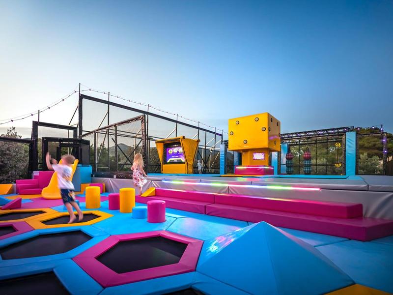 Colorful outdoor play area with trampolines and climbing walls under a blue sky.