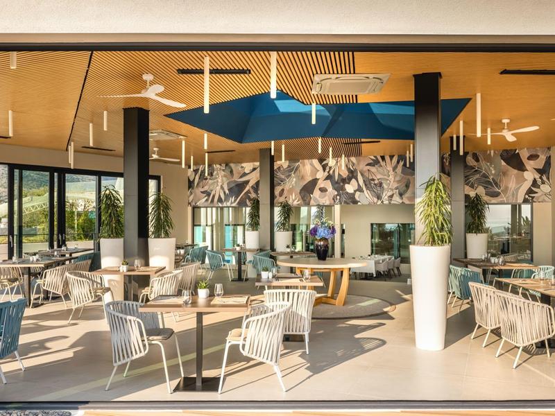Bright modern restaurant with blue accents, white furniture, and large windows.