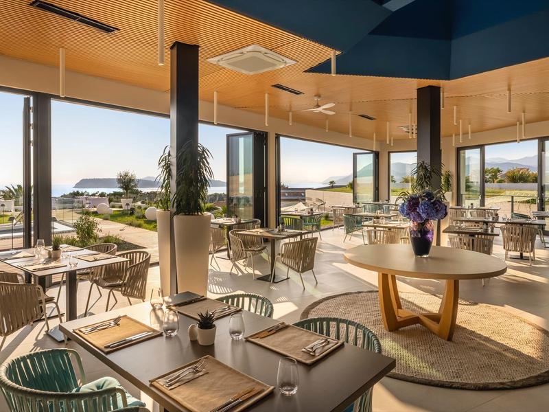 Bright hotel restaurant with wooden ceiling, large windows, modern furnishings, and terrace views.