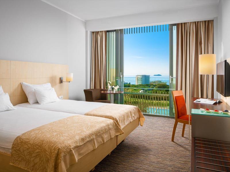 Bright hotel room with two single beds and balcony overlooking the sea