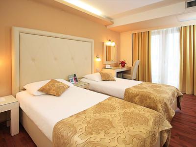 Hotelkamer met twee eenpersoonsbedden, warme kleuren en groot raam met gordijnen.