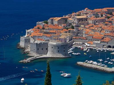 Uitzicht op een kuststad met historische muren, rode daken en een haven met boten.