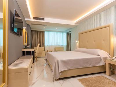 Modernes Hotelzimmer mit großem Bett, Schreibtisch, Fernseher und warmem Licht.