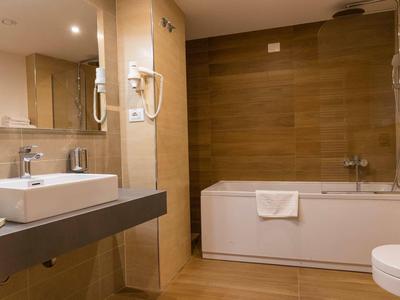 Modernes Badezimmer mit Badewanne, Waschbecken und Haartrockner in warmen Beigetönen.