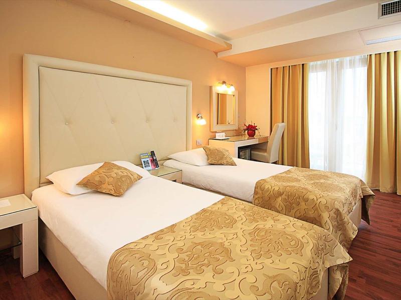 Hotelkamer met twee eenpersoonsbedden, warme kleuren en groot raam met gordijnen.