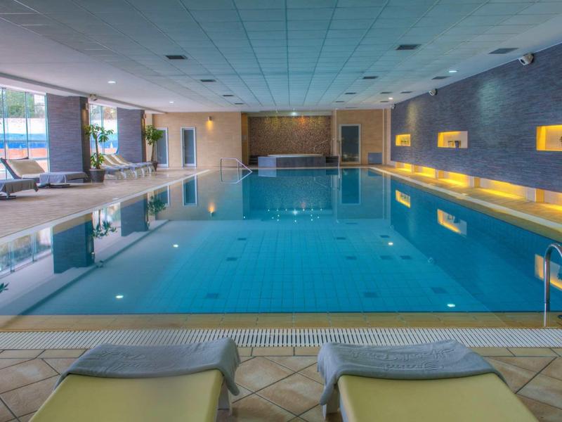 Binnenzwembad van hotel met rustig water, ligstoelen en plafondverlichting.