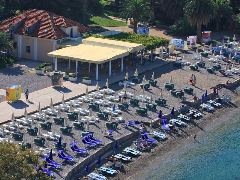 Uitzicht op een strand met ligbedden, parasols en een klein gebouw aan de kust.