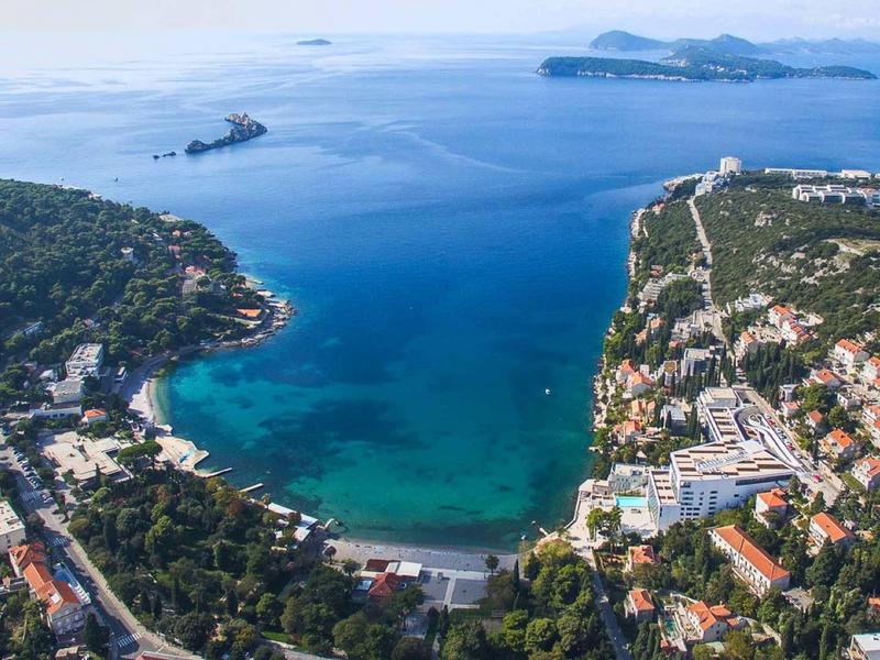 Luchtfoto van een kustplaats met helder blauw water en stranden, omgeven door groene heuvels.