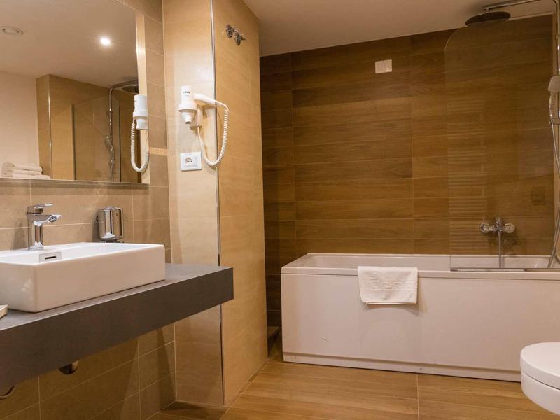 Moderne badkamer met bad, wastafel en grote spiegels in warme kleuren.