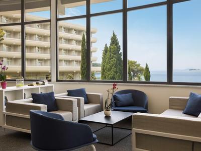 Helle Hotellounge mit Sesseln, Pflanzen und großem Glasfenster mit Meerblick.