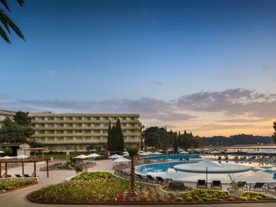 Hotelanlage mit Außenpool, Liegestühlen und Blick auf den Sonnenuntergang.