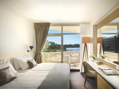 Modernes Hotelzimmer mit Doppelbett, Schreibtisch und Blick auf das Meer durch große Fenster.