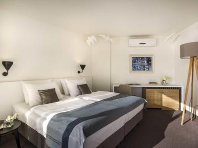 Modern eingerichtetes Schlafzimmer mit großem Bett, Schreibtisch und Stehlampe in neutralen Farben.