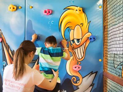 Eine Frau hält ein Kind vor einer farbenfrohen Wand mit Cartoontalent und Angelspiel.