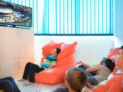 Vier Kinder sitzen auf Bodensitzsäcken und schauen einen Fernseher an, helle Wand und Fenster im Raum.