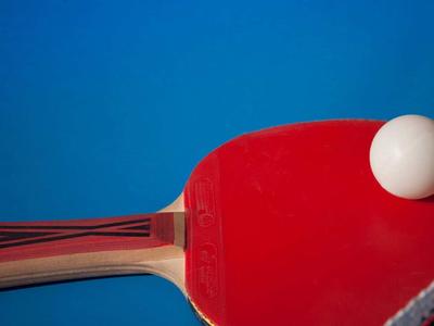 Roter Tischtennisschläger mit weißem Ball vor blauem Hintergrund