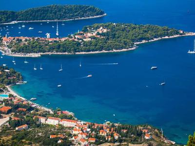 Küste mit blauem Meer, Inseln, Segelbooten und bebauten Uferbereichen in ruhiger Bucht.