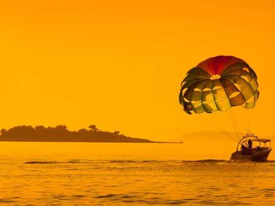 Boot zieht Parasail über gelbem Ozean mit Insel im Hintergrund bei Sonnenuntergang.