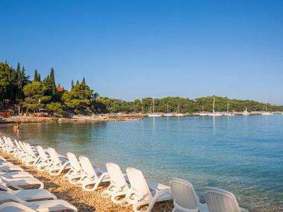 Strand mit weißen Liegestühlen entlang eines ruhigen Meeres unter blauem Himmel