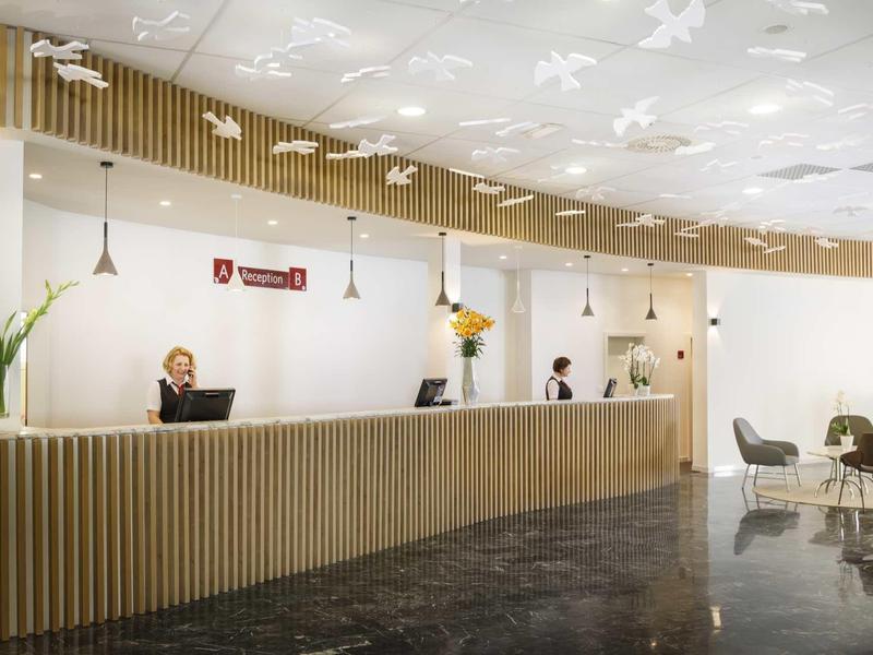 Moderne Rezeption mit langem Holzschalter, weißen Wänden, Blumen und hellem Deckenlicht.