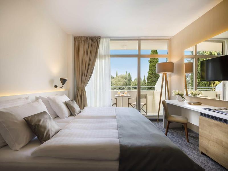 Modernes Hotelzimmer mit großem Bett, Balkon, Fensterfront, Schreibtisch und Fernseher.