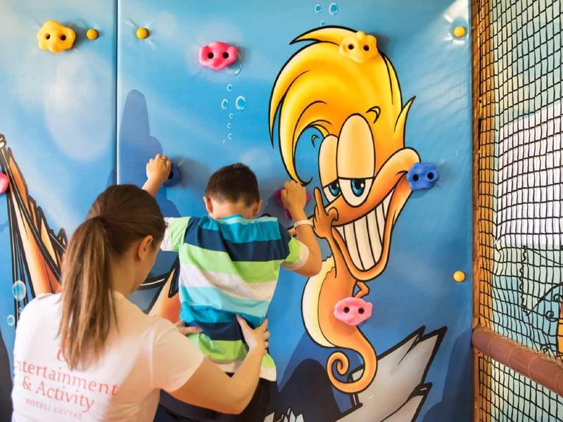 Eine Frau hält ein Kind vor einer farbenfrohen Wand mit Cartoontalent und Angelspiel.