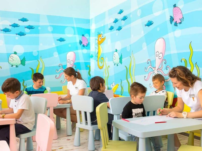 Kinder sitzen an Tischen in einem bunten, mit Meeresmotiven dekorierten Klassenzimmer und lernen.