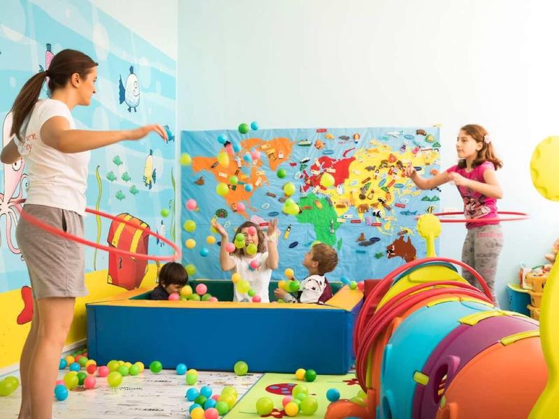 Zwei Frauen spielen in einem bunten, kinderfreundlichen Raum mit Tunnel, Bällen und Weltkarte.