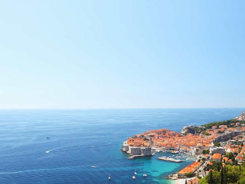 Küste mit orangenen Dächern, blauem Meer und klarem Himmel, Blick auf eine Hafenstadt.