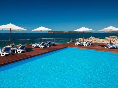 Blauer Außenpool mit Liegestühlen und Sonnenschirmen, Meerblick im Hintergrund.
