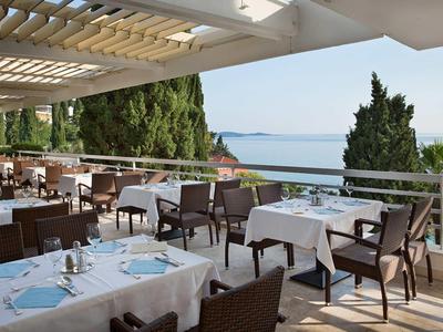 Restaurant terrace with set tables overlooking the sea and green trees.