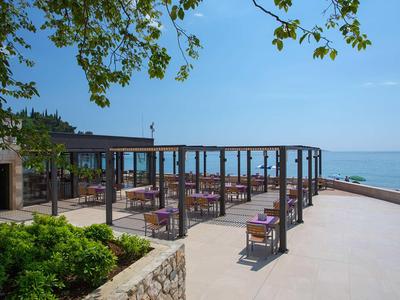 Offene Terrasse eines Restaurants mit Blick aufs Meer, bedeckt von einem Holzgestell und ausgestattet mit Tischen und Stühlen.