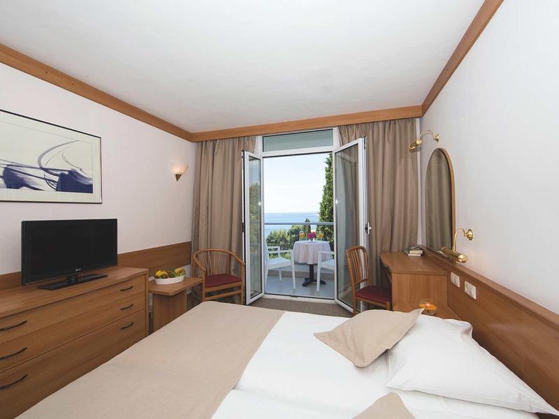 Cozy hotel room with double bed, TV, and balcony overlooking the sea.