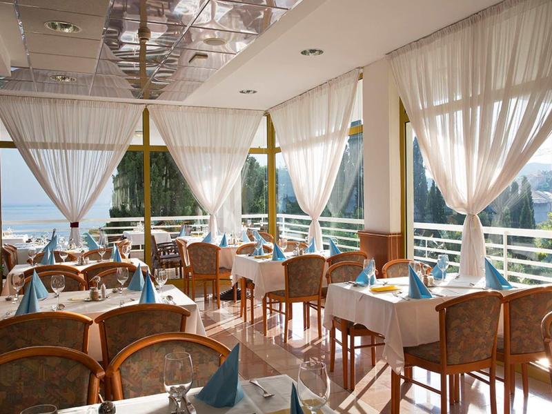 Bright, elegant restaurant with large windows, white curtains, and tables set with blue napkins.