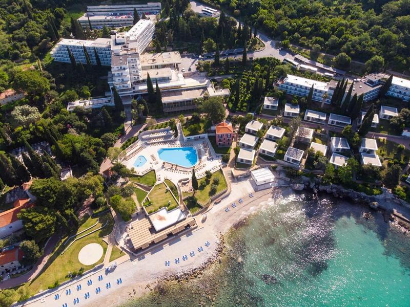 Aerial view of a hotel with pool, beach, and surrounded by lush greenery.