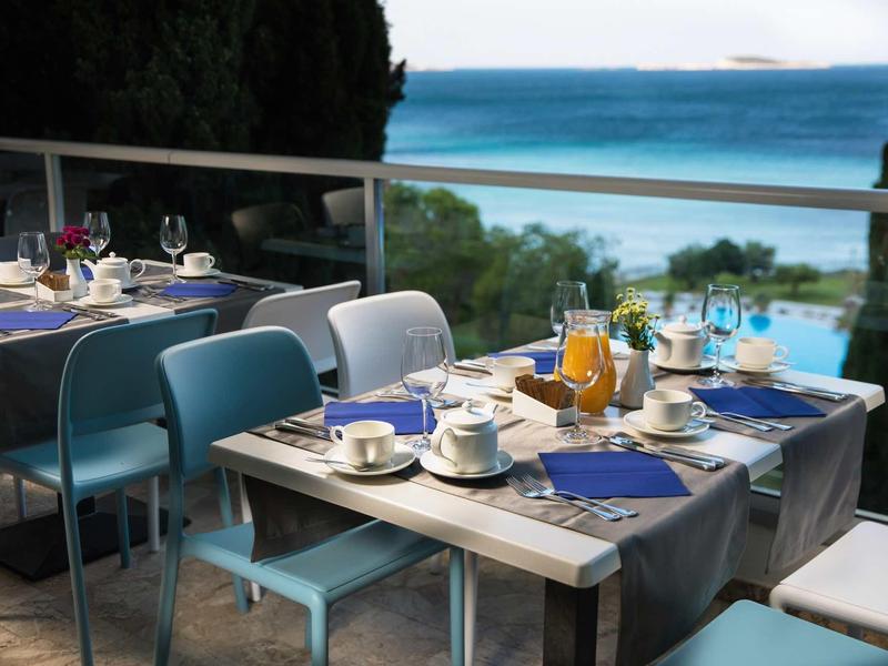Terrace restaurant with blue-gray chairs, set tables, and sea view in the background.