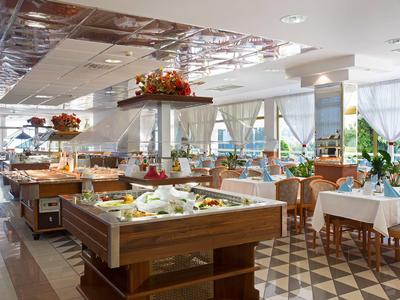 Helles Restaurant mit Buffetbereich und gedeckten Tischen neben großen Fenstern.