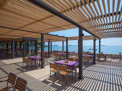 Überdachte Außenterrasse mit Holztischen und Blick auf das Meer bei klarem Himmel.