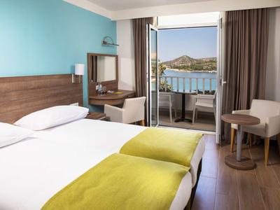 Hotelzimmer mit zwei Betten, Balkon und Blick auf das Meer und Hügel.