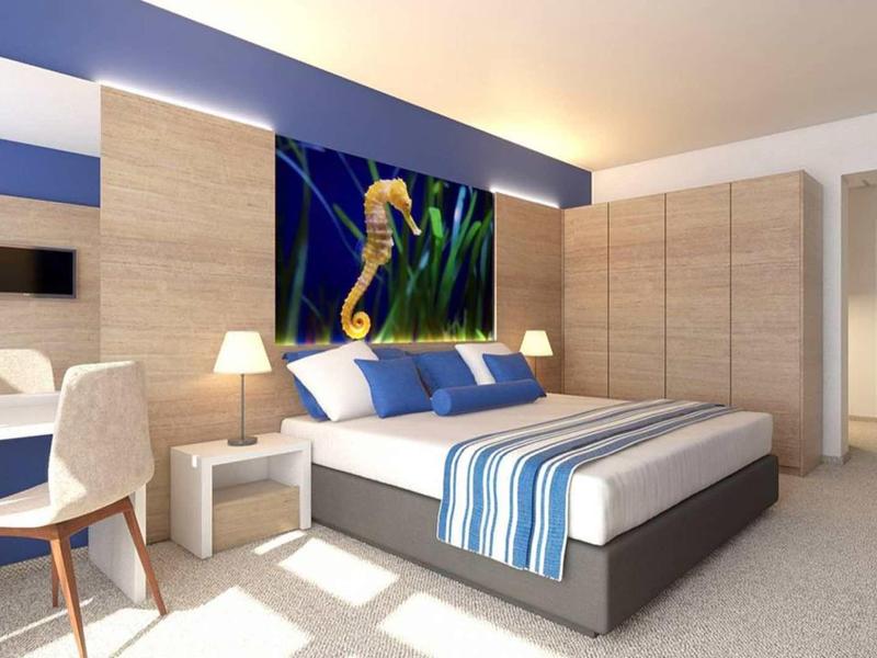 Modern hotel room with double bed, sea creature artwork above it, and a desk with chair.